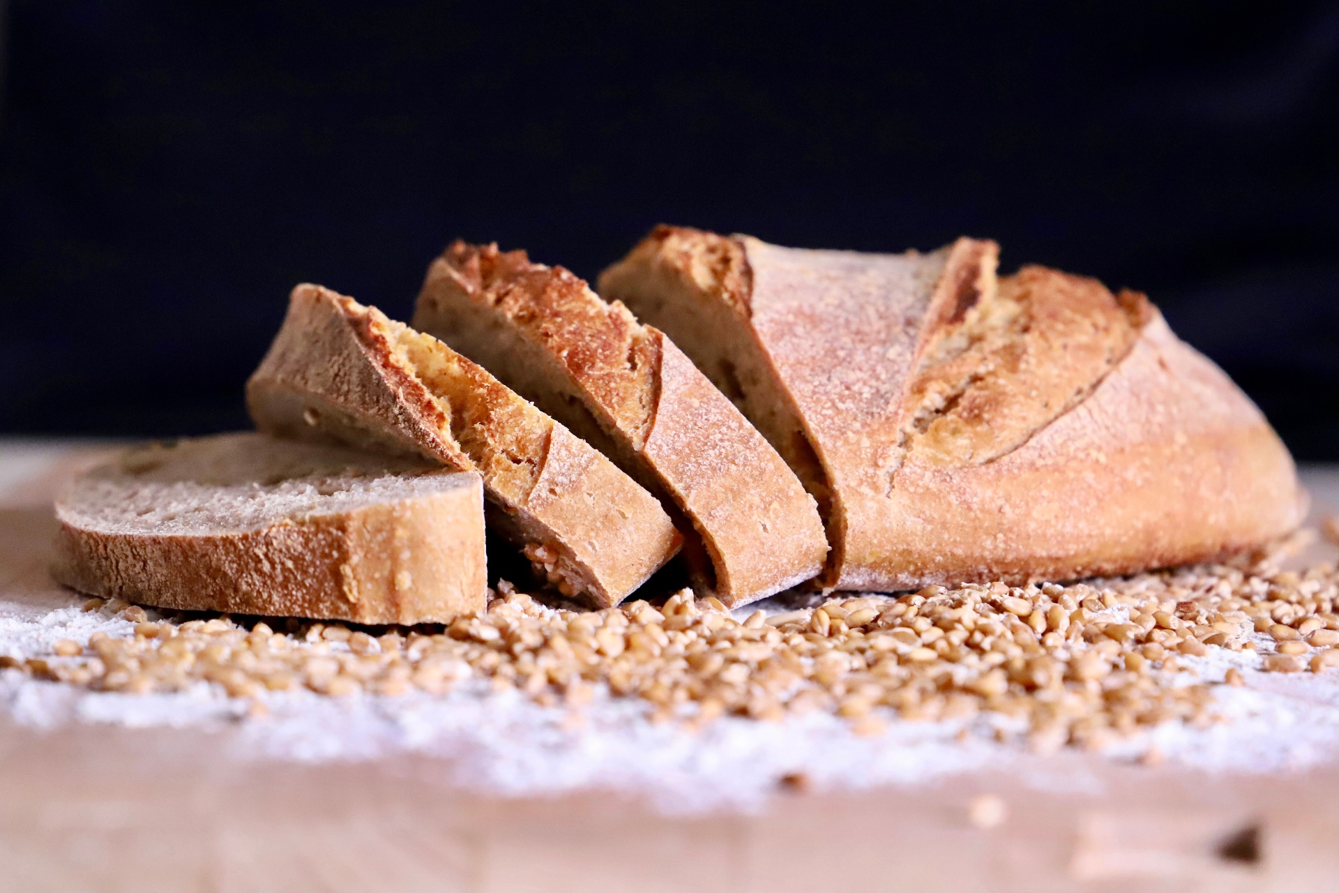 A sliced rustic sourdough loaf resting on wheat grains and a dusting of flour.